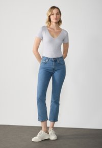 Bodysuit court gris clair à manches courtes, associé �à un jean droit bleu taille haute. Baskets blanches avec des accents beige sur un sol gris.