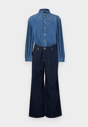 Camisa de ganga com fecho de botões à frente, tecido azul e mangas compridas, combinada com jeans de ganga escura de cintura alta e perna larga. Costuras de contraste visíveis.