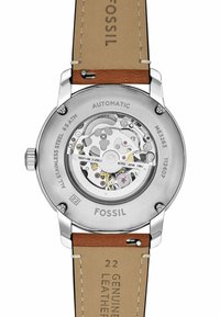Montre automatique en acier inoxydable avec fond transparent laissant apercevoir le mouvement, bracelet en cuir beige, logo Fossil gravé et étanchéité jusqu'à 5 ATM.