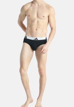 Schwarze Baumwollslips mit einem weißen elastischen Bund, der drei schwarze Streifen aufweist. Figurbetontes Design, glatte Textur und eine vordere Nahtdetails.
