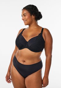 Soutien-gorge nero con dettagli in pizzo sulle coppe, spalline regolabili e banda liscia. Coordina con slip neri a vita alta.
