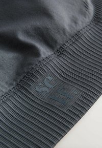 Donkergrijze stof met een textuur van geribde zoom, met een glad logo in een iets donkerdere tint. Het materiaal lijkt zacht en rekbaar.