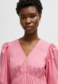 Pink puff sleeve dress with a V-neckline and gathered waistband. Fabric appears smooth, with a lightweight texture and subtle sheen.