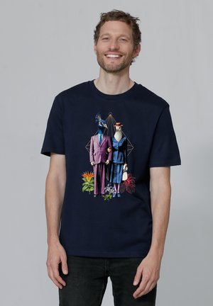 T-shirt en coton bleu marine avec un design graphique de deux oiseaux humanoïdes en tenue formelle, entourés de fleurs tropicales colorées.