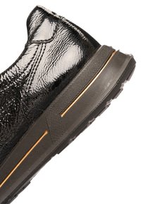 Baskets noires avec une finition vernie brillante, des zones texturées, une semelle en caoutchouc solide avec des accents orange, et une forme profilée.