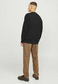 Felpa nera e pantaloni marroni, con una vestibilità rilassata, collo a giro, polsini a coste e tessuto testurizzato. Scarpe marroni completano il look.