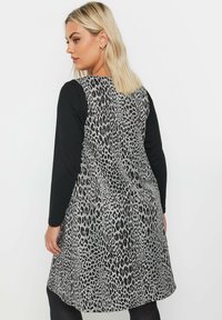 Schwarzes Langarmoberteil mit einem knielangen Kleid, das ein Leopardenmuster in Grautönen und Silber zeigt, eine glatte Textur hat und figurbetont geschnitten ist.