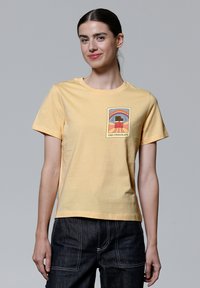 Geel T-shirt met korte mouwen van katoen, met een bedrukte afbeelding van een taart en een regenboog aan de voorkant. Rechte pasvorm met een ronde halslijn.
