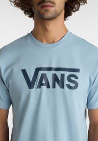 Tyrkysové bavlněné tričko s velkým tmavě modrým logem "VANS", umístěným uprostřed hrudi. Standardní kulatý výstřih a krátké rukávy.