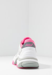 Baskets blanches avec un talon gris et des accents roses. Dotées d'un col rembourré, de matériaux texturés et d'une semelle en caoutchouc avec une bande de roulement prononcée.