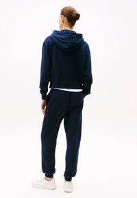 Sweat-shirt bleu marine avec un design cropped, doté d'une capuche et de manches longues, accompagné de pantalons jogging assortis et de baskets blanches.