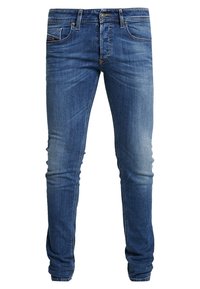 Vaqueros de denim azul con un corte ajustado, que presentan un desvanecimiento sutil y detalles de desgaste. Diseño de cinco bolsillos con herrajes de metal y acentos cosidos.