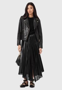 Musta nahkainen biker-takki kultaisilla koristeilla, musta neulepaita, laskostettu musta hame ja mustat remmisandaalit. Kapealahkeinen, kiiltävä pinta.