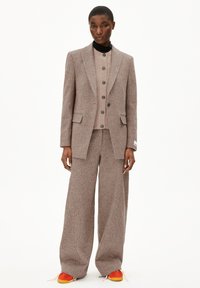 Getextureerde brown blazer en bijpassende wijde broek, gelaagd over een crèmekleurig gebreid top met knopen, gecombineerd met opvallende sneakers in oranje en geel.
