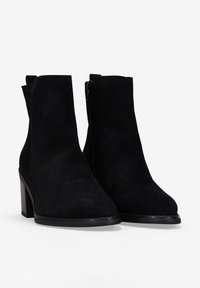 Botines de ante negros con un alto tacón cuadrado. Las características incluyen una textura suave, una punta redondeada y un cierre de cremallera lateral.