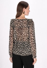 Blusa nera trasparente con stampa leopardata in beige. Collo e polsini arruffati, maniche lunghe, vestibilità fluida, abbinata a pantaloni neri semplici.
