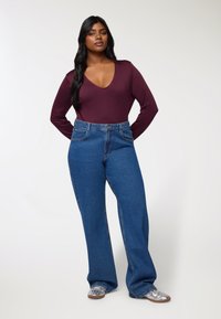 Bordowy bodysuit z długim rękawem i głębokim dekoltem w kształcie litery V, w połączeniu z niebieskimi dżinsami o szerokich nogawkach z wysokim stanem. Srebrne buty dopełniają stylizację.