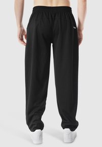 Schwarze, gerippte Sweatpants mit elastischem Bund, mit seitlichen Nähten und kleinem Logo, kombiniert mit weißen Sneakern.