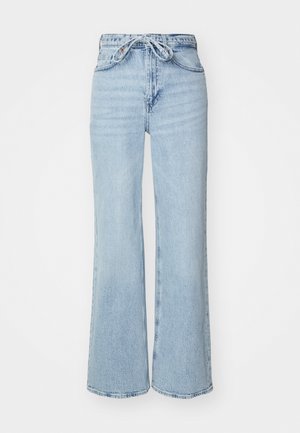 Lys blå denimjeans med bred benform, høy midje og snorforbindelse. Har en teksturert finish og rå kant.