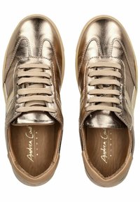 Sneakers metallici oro e beige con tomaia in pelle liscia, lacci piatti e suola in gomma leggera. L'interno presenta una soletta marrone con logo stampato.