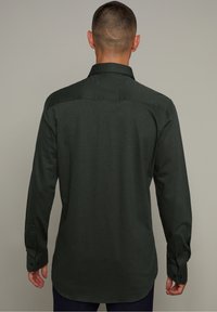 Camicia verde scuro con bottoni, maniche lunghe, tessuto testurizzato, dettaglio sul retro, orlo arrotondato, con bottoni e polsini neri.