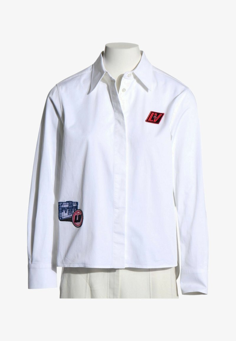 Chemise blanche à manches longues avec col et boutons, décorée de patchs rectangulaires rouges et bleus sur la poitrine et la partie basse avant.