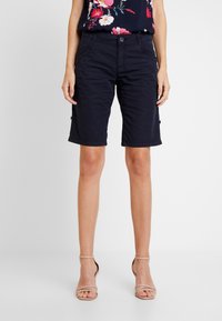 Marinblå bomullsshorts med figursydd design, knälånga, med fickor fram och sidofickor i cargostil. Texturerat tyg med sömdetaljer.