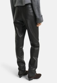 Schwarze Lederhosen mit glatter Textur, verfügt über Gesäßtaschen und ein figurbetontes Design. Tragen mit einem grauen Pullover und dunklem Schuhwerk.