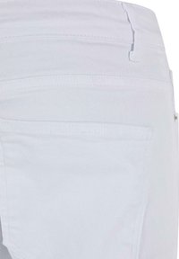 Jeans de mezclilla blanca con una textura suave, corte slim y detalles en los bolsillos traseros con costuras sutiles y bordes limpios.