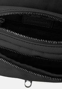 Interno di una borsa nera con cerniera, arricchito da dettagli in pelle nera texturizzata. Più scomparti con cerniere tono argento e un rivestimento in tessuto.