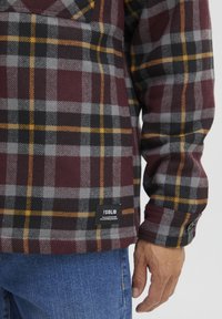 Geruite flanellen overhemd in bordeauxrood, grijs en zwart met gele accenten. Voorzien van een borstzak en een label op de onderste zoom. Met knoopmanchetten.