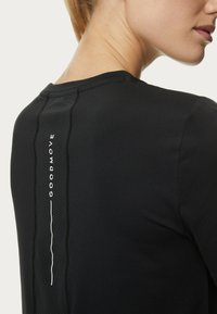Camiseta deportiva negra con una textura suave, que presenta un panel de malla y la marca "GOODMOVE" a lo largo de la parte posterior. Diseño de mangas cortas.