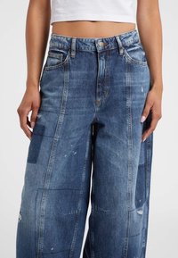 Denim-Hosen mit weitem Bein in einem blassen Blauton, ausgestattet mit Patches, Waschungen und einer lockeren Silhouette. Vordertaschen sind enthalten.