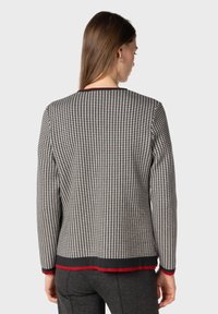 Cardigan in wool con un motivo a scacchi bianco e nero, caratterizzato da un bordo rosso lungo il colletto e l'orlo, e maniche lunghe.