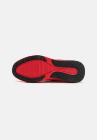 Rød sneakersåle med teksturert sort gummitread og en jevn rød mellomsåle. Har spor for grep og stabilitet.