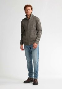 Grå zip-up tröja med ribbad detalj på axlarna, bärs över ljusblå jeans och bruna stövlar; slät stickad struktur och figursydd design.