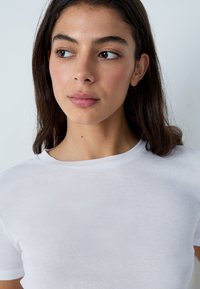 Camiseta blanca de manga corta hecha de una tela suave y ligera. Presenta un clásico cuello redondo y una textura suave sin patrones ni adornos.
