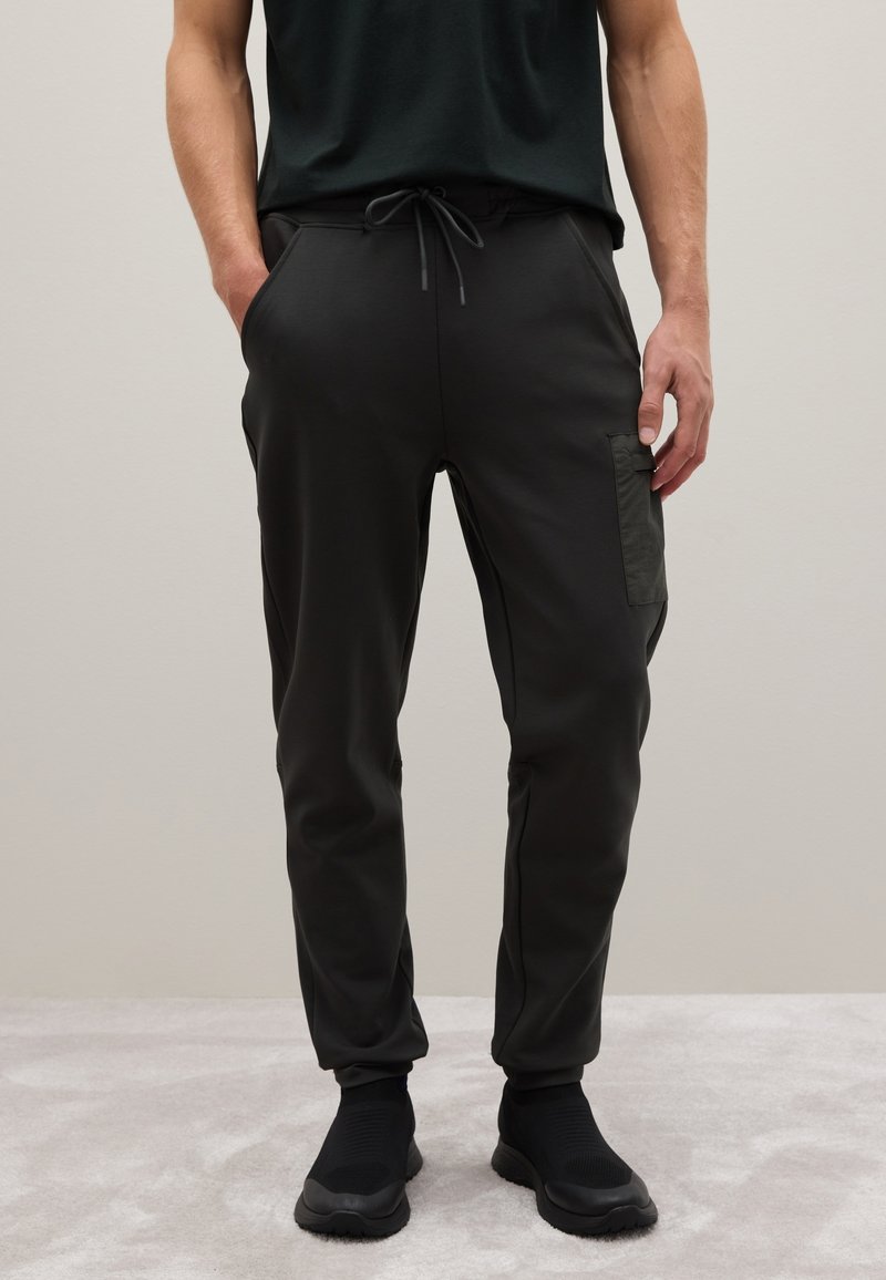 Schwarze Sporthosen mit einem elastischen Kordelzugbund, schmal zulaufenden Beinen und einer seitlichen Taschen aus einem glatten, leichten Material.