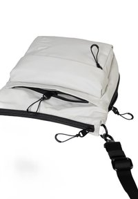 Borsa di tessuto bianco con design trapuntato, dotata di tasca con zip, accenti neri e tracolla regolabile con clip. Stile minimalista.