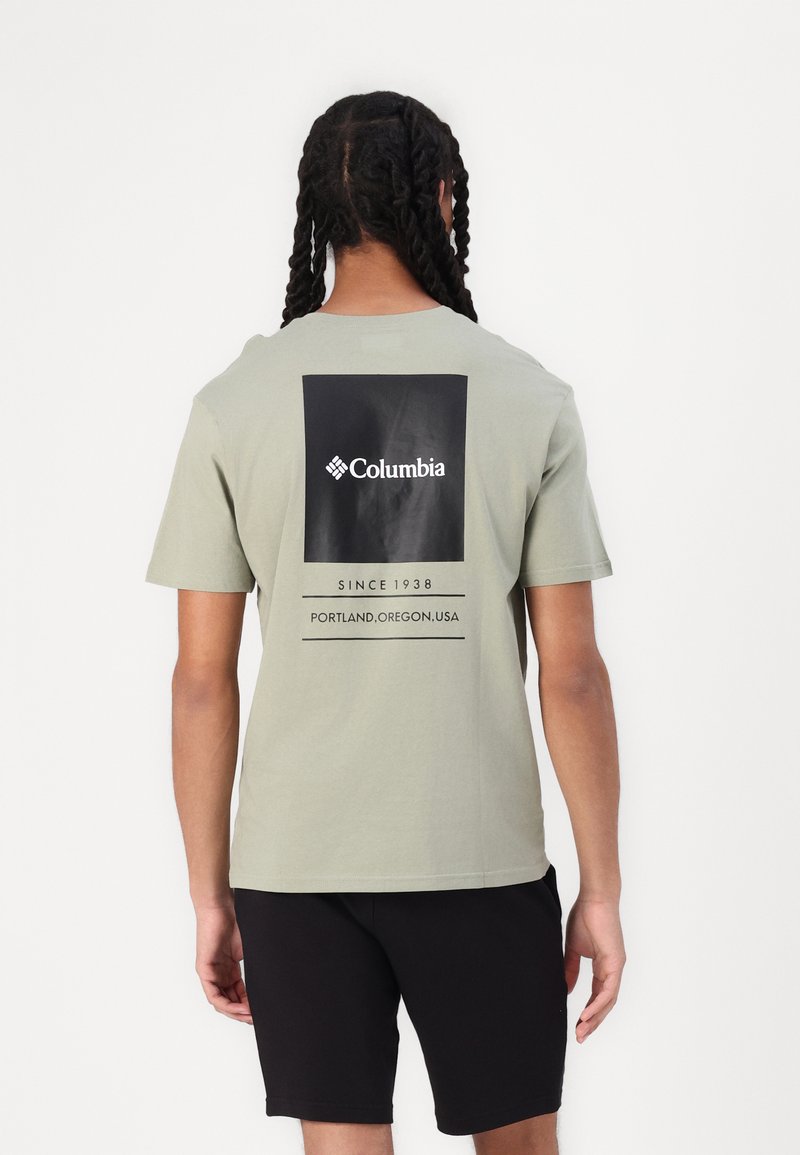 Olivengrøn bomulds t-shirt med et sort rektangulært logo på ryggen med hvid tekst. Kombinationen er med sorte shorts.