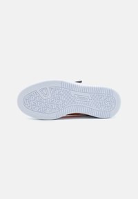 Semelle de sneaker blanche avec une texture antidérapante, comportant un logo en relief et un motif géométrique. Le bord est légèrement surélevé pour plus de stabilité.