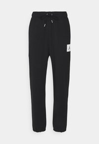 Pantalones de chándal negros de tejido suave, con cinturilla elástica y cordón, piernas ajustadas y un pequeño parche de logo en el lado izquierdo.