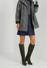 Rutig ytterkläder i grått och svart, ihopparat med en marinblå mockaskjol. Gröna knähöga stövlar med dragkedjedetalj fulländar looken.