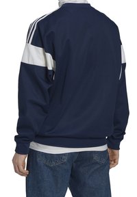 Marinblå sportjacka med vita ränder över axlarna. Tillverkad av mjukt tyg, med en avslappnad passform och ribbade muddar.