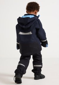 Navy and black rain jacket with a hood, featuring blue accents and reflective stripes. Worn with matching black pants and black shoes.