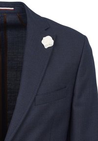 Blazer navy con un tessuto testurizzato, presenta un bottone a fiore bianco come distintivo, una tasca sul petto singola e una fodera interna marrone.