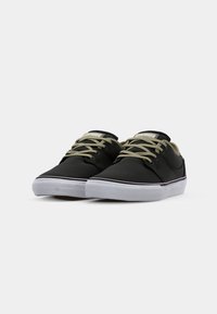 Black canvas sneakers with beige laces and logo, white rubber sole, rounded toe, and subtle side stitching detail.