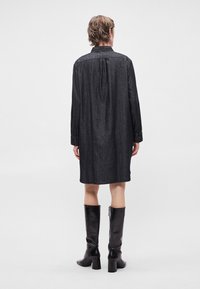 Σκούρο τζιν φόρεμα πουκάμισο με μακριά μανίκια, πίσω γιακά και ίσια γραμμή. Συνδυάζεται με μαύρες δερμάτινες μπότες μέχρι το γόνατο με τακούνι.