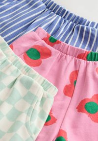 Tre paia di pantaloni corti a fantasia: blu con righe bianche, rosa con fiori rossi e centri verdi, e tessuto a quadretti verde menta.