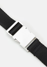 Zwarte webbingriem met een zilveren metalen gesp. De gesp heeft een rechthoekige vorm met gladde randen. De riem heeft een gestructureerd oppervlak.
